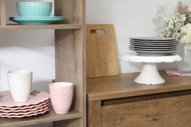 Beyaz duvarın yanında farklı bulaşık takımları ve fincanlar olan raf ünitesi.