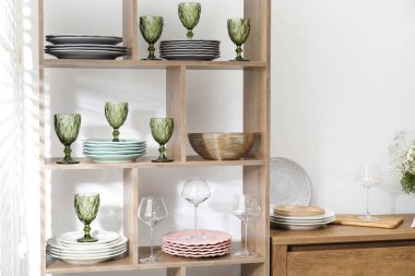 Beyaz duvarın yanında farklı bulaşık takımları ve gözlüklerle raf ünitesi.