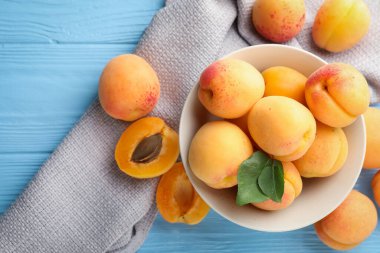 Açık mavi ahşap masa üzerinde yeşil yapraklı taze kayısılar.