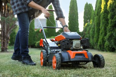 Bahçedeki çim biçme makinesinin marş kablosunu çeken adam, yakın plan.