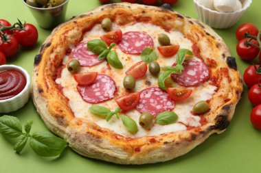 Yeşil masada salamlı, zeytinli, domatesli ve fesleğenli lezzetli pizza.