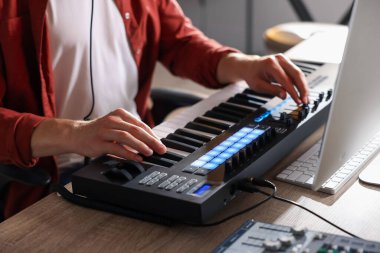 İçerideki ahşap masada MIDI klavyesiyle çalışan adam, yakın plan.