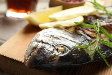 Ahşap masada biberiye ve limonla servis edilen kızarmış dorado balığı, yakın plan. Ev yapımı deniz ürünleri yemeği.