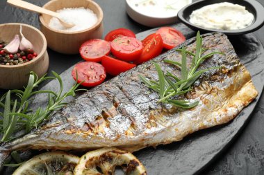 Lezzetli kızarmış uskumru, siyah masada baharat ve sosla servis ediliyor, yakından. Ev yapımı deniz ürünleri yemeği.