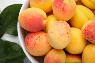 Tabakta taze kayısılar ve masada yeşil yapraklar.