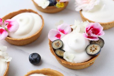 Lezzetli tatlı. Kremalı tartlar, böğürtlenler ve çiçekler beyaz döşemeli masada, yakın plan.
