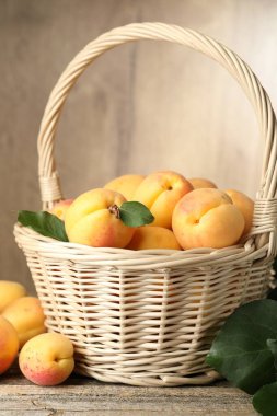 Hasır sepette taze kayısılar ve ahşap masada yeşil yapraklar, yakın plan.