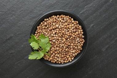 Kişniş tohumu ve taze kişniş yaprakları koyu dokulu masada, üst tarafta.