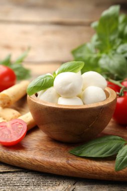 Lezzetli mozzarella peyniri topları, domatesler, fesleğen ve grissini ahşap masada, yakın plan.