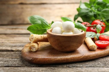 Lezzetli mozzarella peyniri topları, domatesler, fesleğen ve grissini ahşap masada, yakın plan.