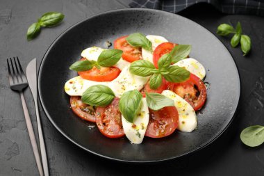 Mozzarella, domates, fesleğen ve baharatlarla siyah masaya yakın plan Caprese salatası.