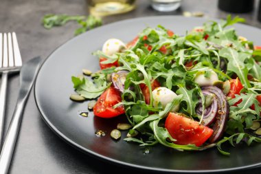 Lezzetli salata roka, mozzarella ve sebzeler gri masada servis edilir, yakın plan.