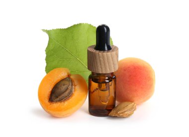 Bir şişe temel yağ, taze kayısılar, çekirdekler ve beyaz üzerine izole edilmiş yeşil yaprak.