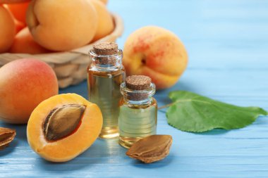 Yağ şişeleri, taze kayısılar ve açık mavi ahşap masa üzerindeki çekirdekler, yakın plan. Metin için boşluk