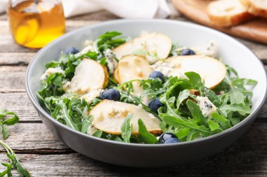 Lezzetli salata roka, armut, mavi peynir, fıstık ve yabanmersinleri ahşap masada, yakın plan.