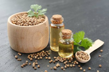 Şişelerdeki Aromatik yağ, kişniş yaprakları, kase ve kaşık dolusu kişniş tohumları koyu dokulu masa, yakın çekim