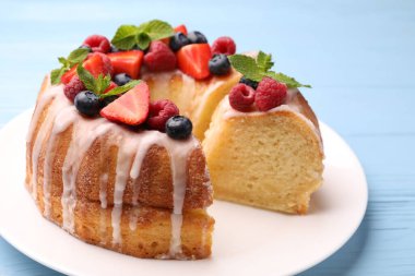 Lezzetli meyveli kek parçaları, açık mavi ahşap masa üzerinde jöle ve nane, yakın plan.