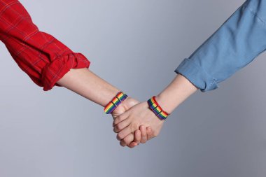 LGBT konsepti. Gökkuşağı bileklikli kadınlar açık gri arka planda el ele tutuşuyorlar, yakın plan.
