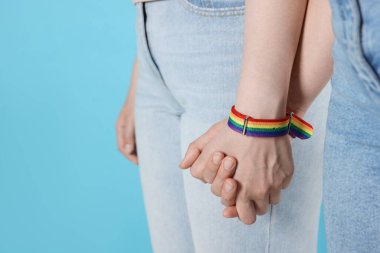 LGBT konsepti. Gökkuşağı bileklikli kadınlar açık mavi arka planda el ele tutuşuyorlar, yakın plan. Metin için boşluk