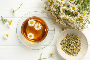 Cam bardakta Aromatik çay ve beyaz ahşap masada papatya çiçekleri.
