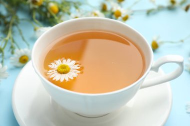 Lezzetli papatya çayı ve açık mavi arka planda çiçekler, yakın plan.