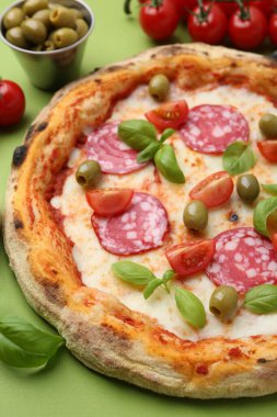 Yeşil masada salamlı, zeytinli, domatesli ve fesleğenli lezzetli pizza.