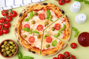 Açık yeşil arka planda leziz kesilmiş pizza ve malzemeler.