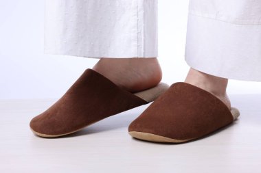 Açık ahşap zeminde, yumuşak kahverengi terlikli kadın beyaz arka planda, yakın plan.