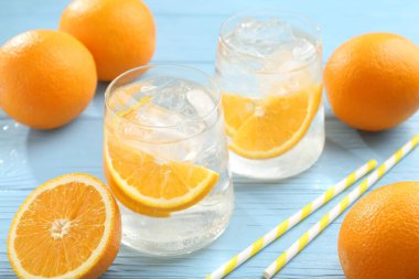 Portakal dilimli maden suyu, taze meyve ve pipetler açık mavi ahşap masada, yakın plan.