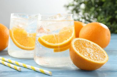 Portakal dilimli maden suyu, taze meyve ve pipetler açık mavi ahşap masada, yakın plan.