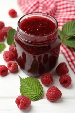 Lezzetli reçel, taze ahududu ve yapraklar beyaz ahşap masada, yakın plan.