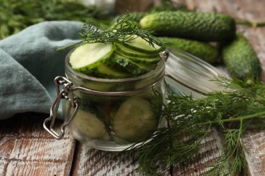 Turşu yapıyorum. Açık kavanozda taze salatalık dilimleri ve ahşap masa üzerinde dereotu, yakın plan.