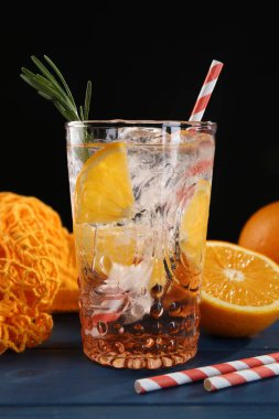 Bardakta portakallı maden suyu, mavi ahşap masada taze meyve ve pipetler, yakın plan.