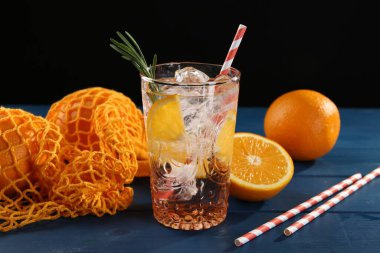 Bardakta portakallı maden suyu, mavi ahşap masada taze meyve ve pipetler, yakın plan.