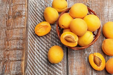 Tahta masanın üzerinde hasır sepetin içinde taze olgun kayısılar, düz uzanmış. Metin için boşluk