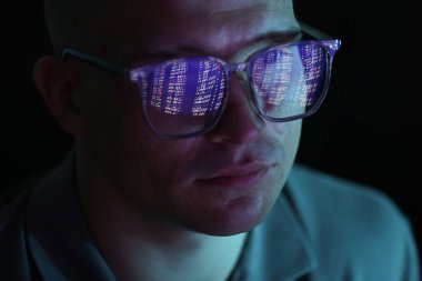 Siyah arka planda yansıması olan gözlüklü genç adam, yakın plan.