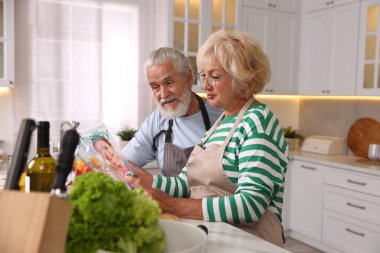 Yaşlı çift mutfakta birlikte dergi okuyor.