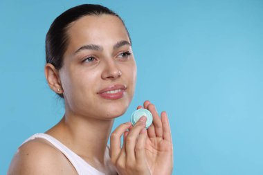 Açık mavi arkaplanda dudak kremi olan genç bir kadın, mesaj için yer var.