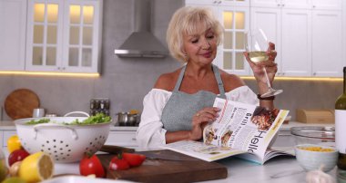 Son sınıf öğrencisi kadın dergi okuyor ve mutfakta beyaz şarap içiyor.