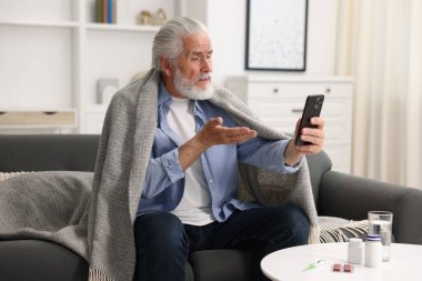 Üst düzey bir adam, evdeki akıllı telefondan doktorla çevrimiçi görüşme yapıyor.