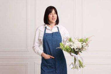 Beyaz duvarın yanında güzel çiçek buketi olan bir çiçekçi.