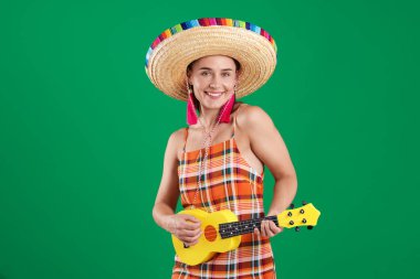 Yeşil arka planda ukulele çalan şapkalı gülümseyen kadın.