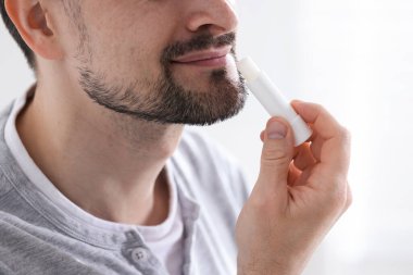 Bulanık ışık arka planında dudaklarına dudak kremi süren bir adam.