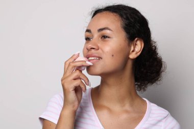 Gülümseyen kadın gri arka planda dudaklarına merhem sürüyor.