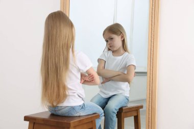 Üzgün küçük kız aynada kendine bakıyor.