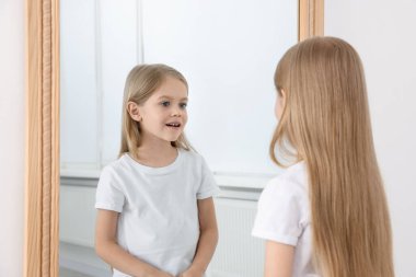 Güzel küçük kız aynada kendine bakıyor.