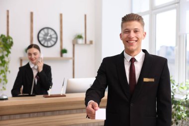 Üniformalı bir resepsiyonist anahtar kartı veriyor ve iş arkadaşı otelde çalışıyor, seçici bir şekilde.