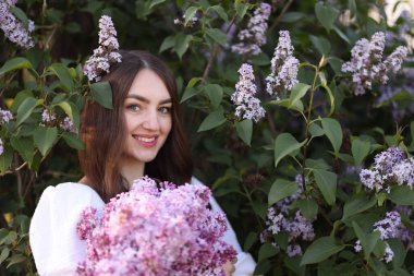 Leylak çiçeklerinin arasında gülümseyen ve açık havada terk eden kadın.