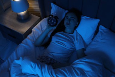 Alarmlı saati olan hayal kırıklığına uğramış bir kadın evinde, yatağında uykusuzluk çekiyor.