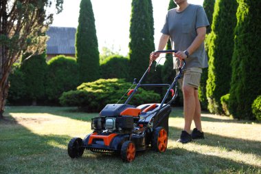 Bahçede çim biçme makinesiyle çimen biçen adam, yakın plan.